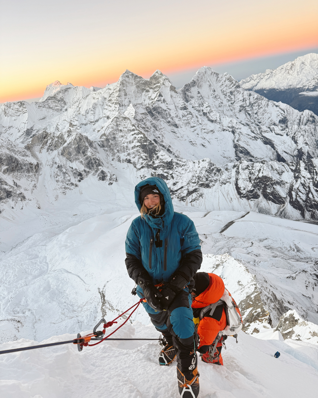 Person in winter gear on a snowy mountain with a sunset in the background