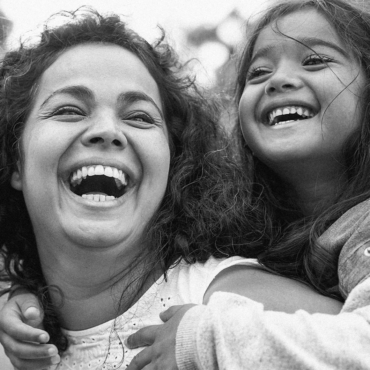 Black and white close-up photograph of a woman and a young girl laughing together outdoors.