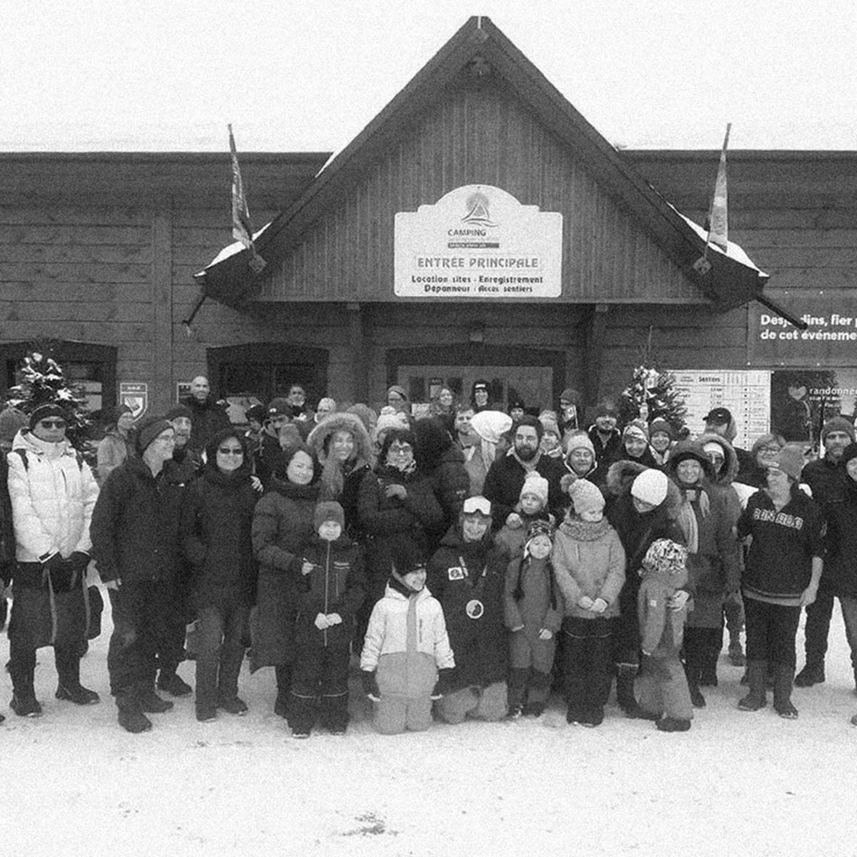 A black and white group photograph of people standing in front of a large wooden building with a sign reading 'ENTREE PRINCIPALE' and 'Sévérengis'.